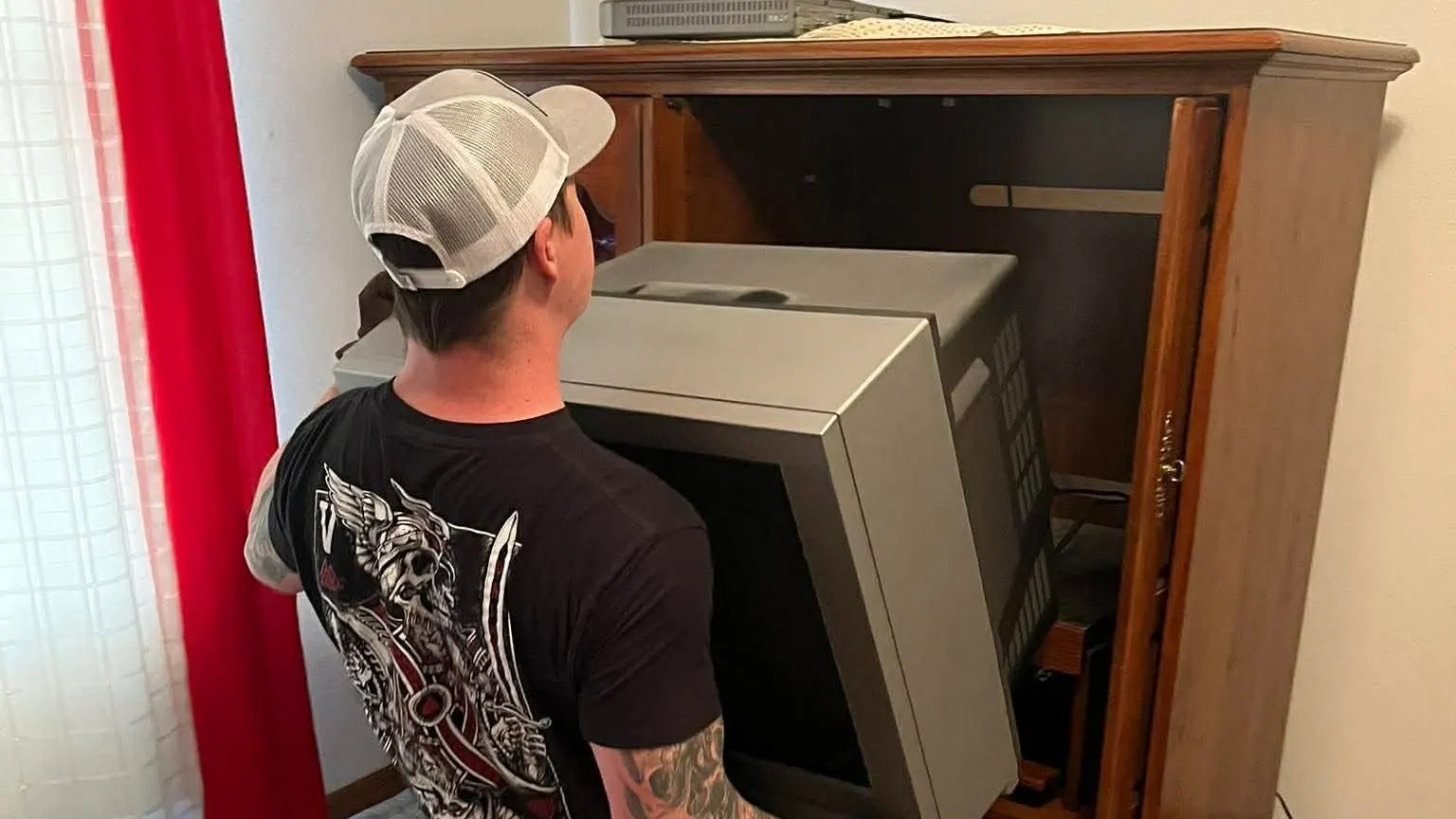 The owner lifting an old tube TV out of a wooden entertainment cabinet
