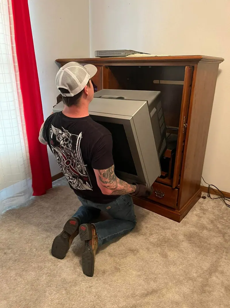 The owner lifting an old tube TV out of a wooden entertainment cabinet