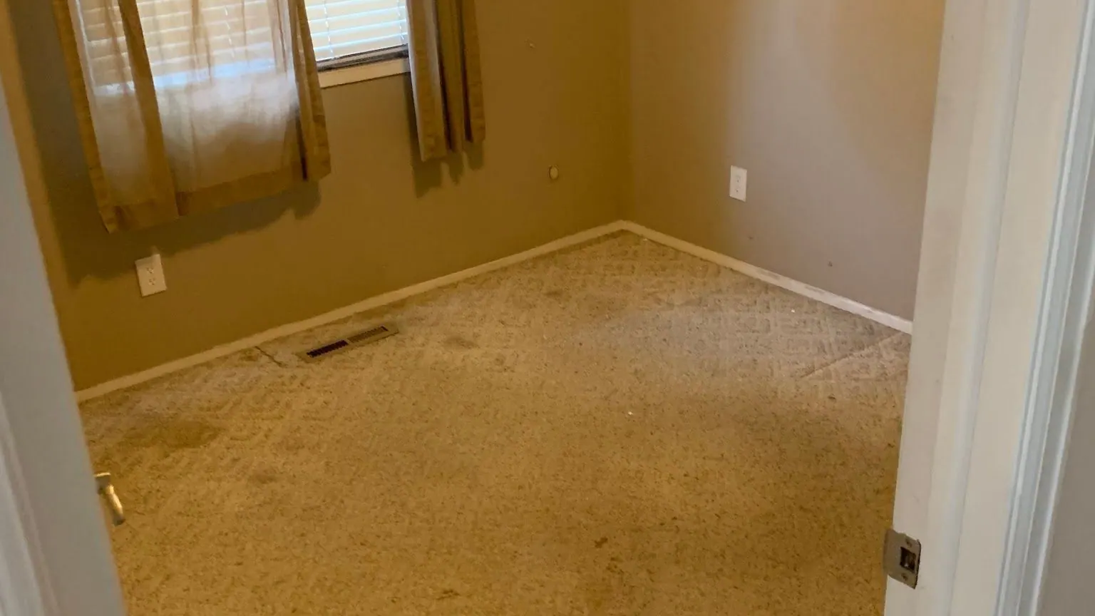 An empty carpeted bedroom with a window and a ceiling light