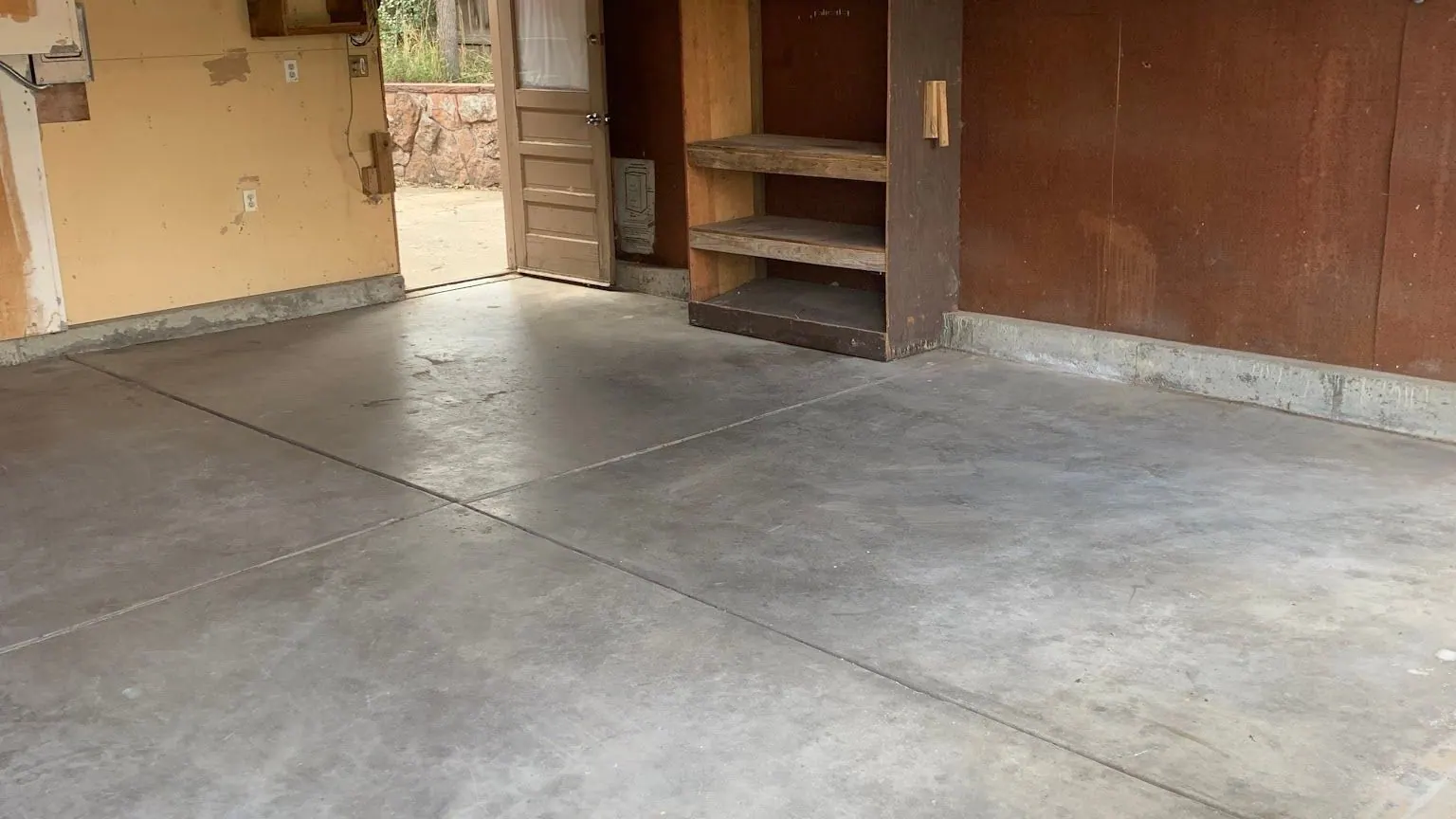 An empty garage with a clean concrete floor and built-in wood shelving