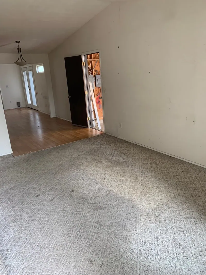 An emptied living room with patterned carpet and a laminate floor beyond