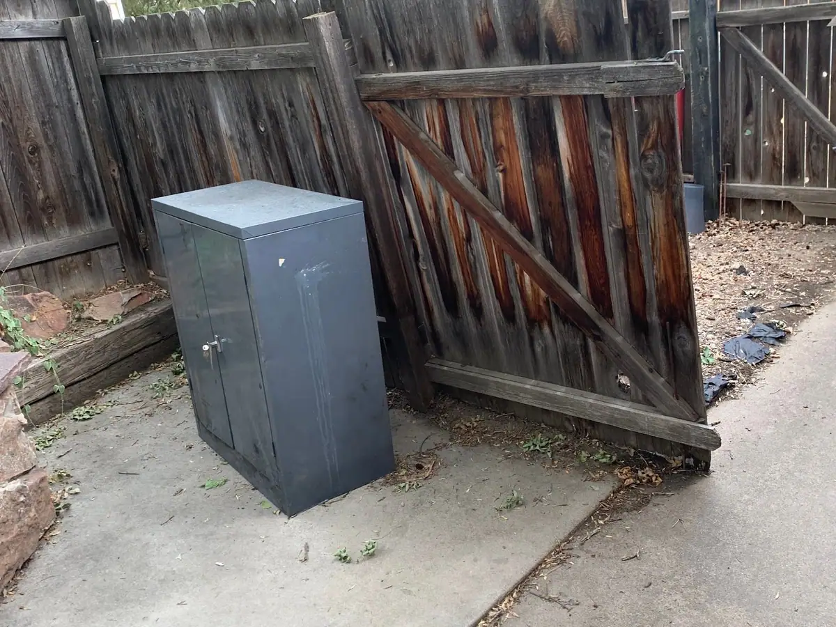 A steel storage cabinet on a concrete pad by a wood fence