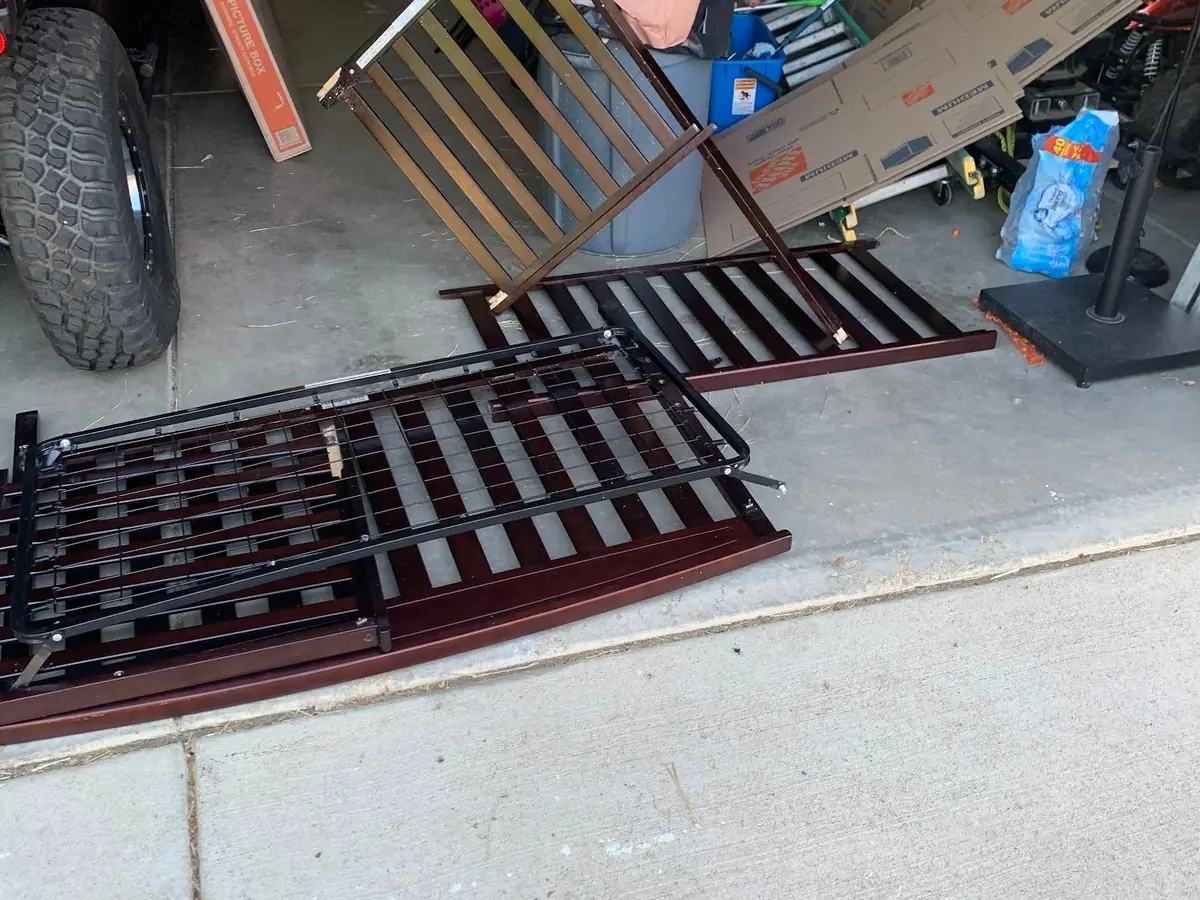 A garage with a dark wood crib taken apart on the floor