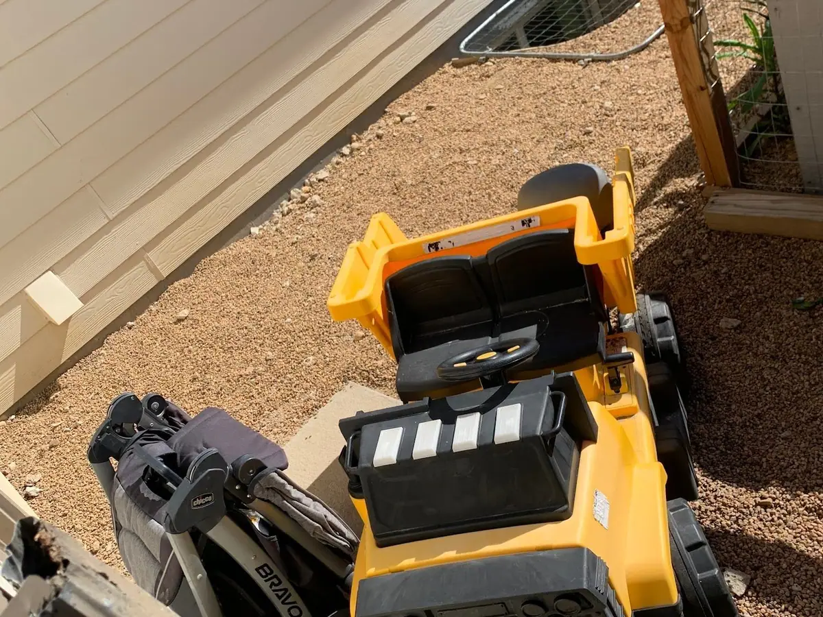 A kid's ride-on truck and a stroller in a narrow side yard