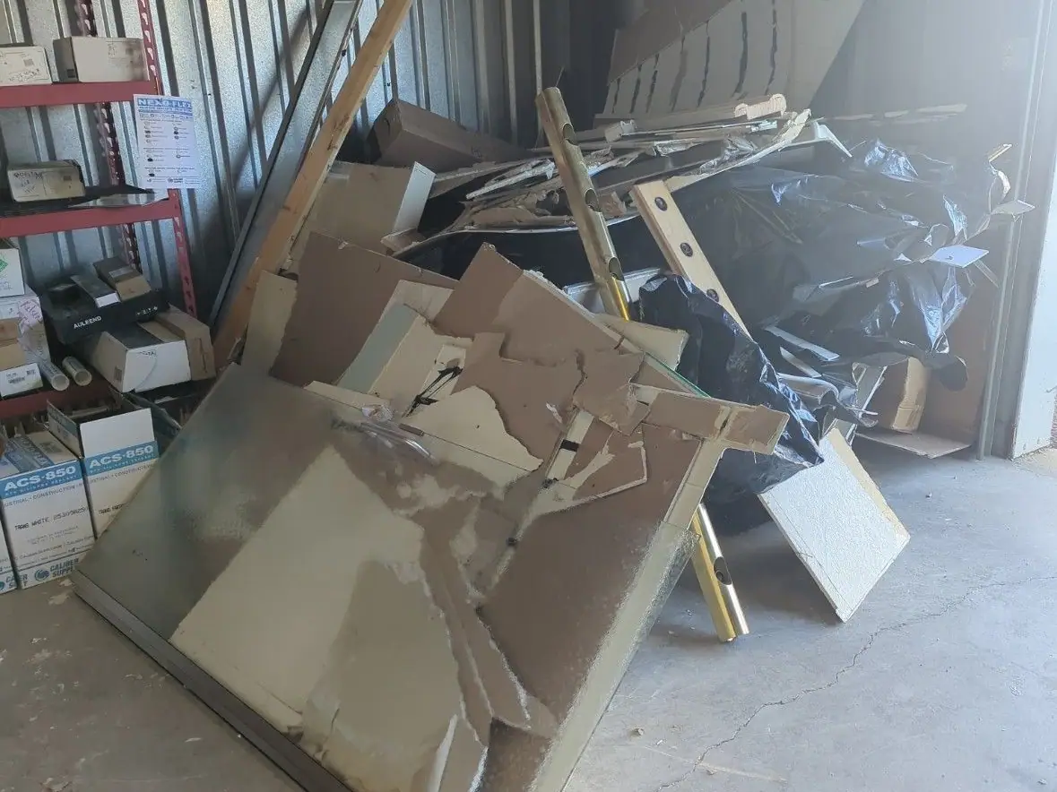 A storage unit with broken drywall and a glass panel stacked against the walls