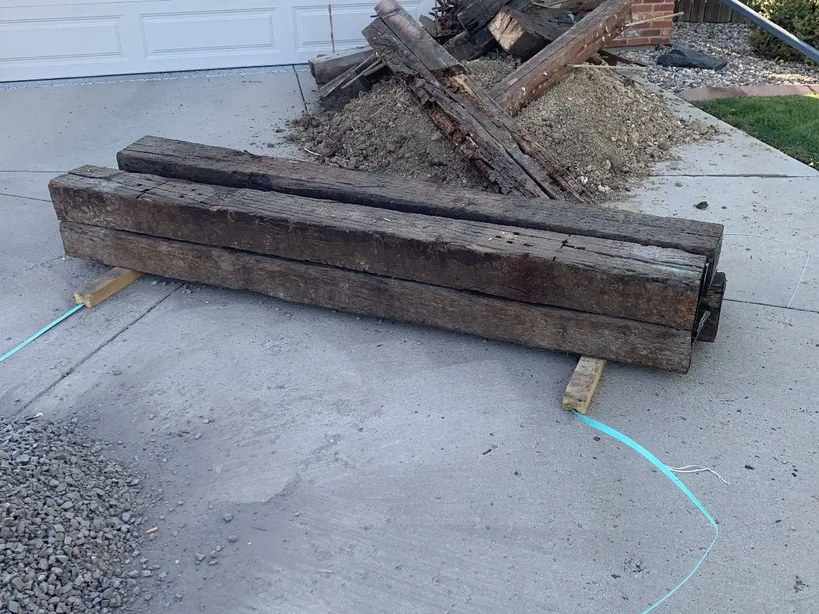 Old railroad ties and a pile of fill dirt on a driveway in front of a garage door