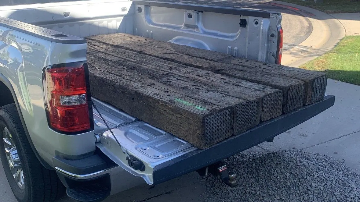 Old wooden beams stacked on the open tailgate of a silver GMC pickup