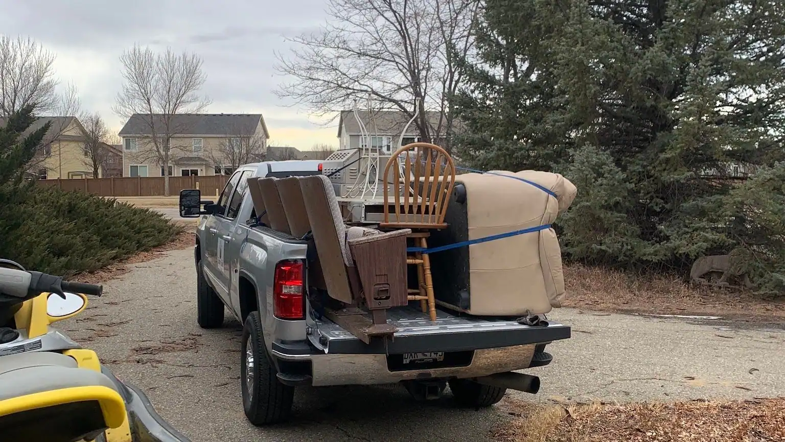 A tan couch and a wooden chair strapped into the bed of a silver GMC pickup