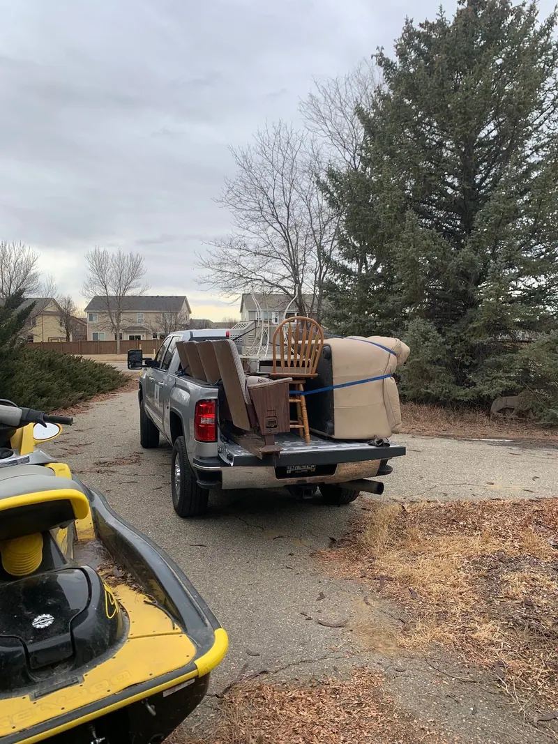 A tan couch and a wooden chair strapped into the bed of a silver GMC pickup