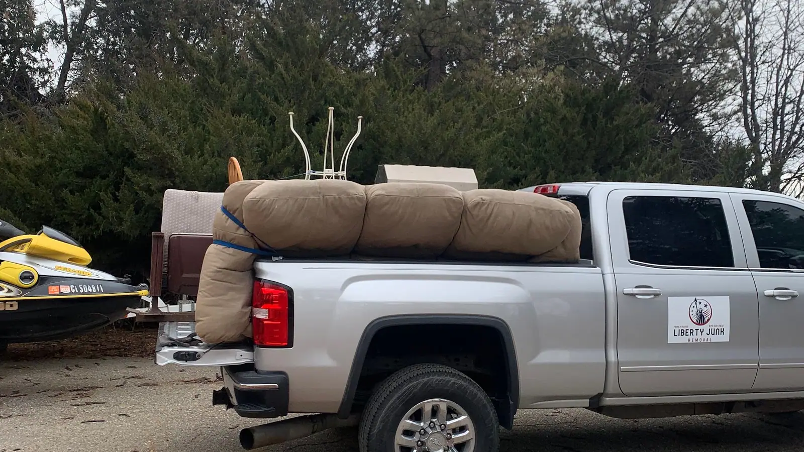A couch and cushions loaded on a silver GMC pickup with the Liberty Junk Removal sign on the door