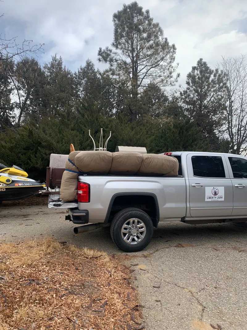 A couch and cushions loaded on a silver GMC pickup with the Liberty Junk Removal sign on the door