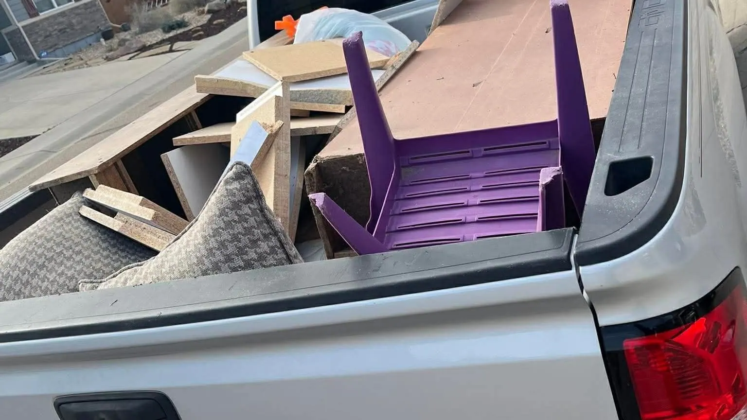 Couch cushions, flat cardboard, scrap boards and a purple chair in the bed of a silver GMC pickup