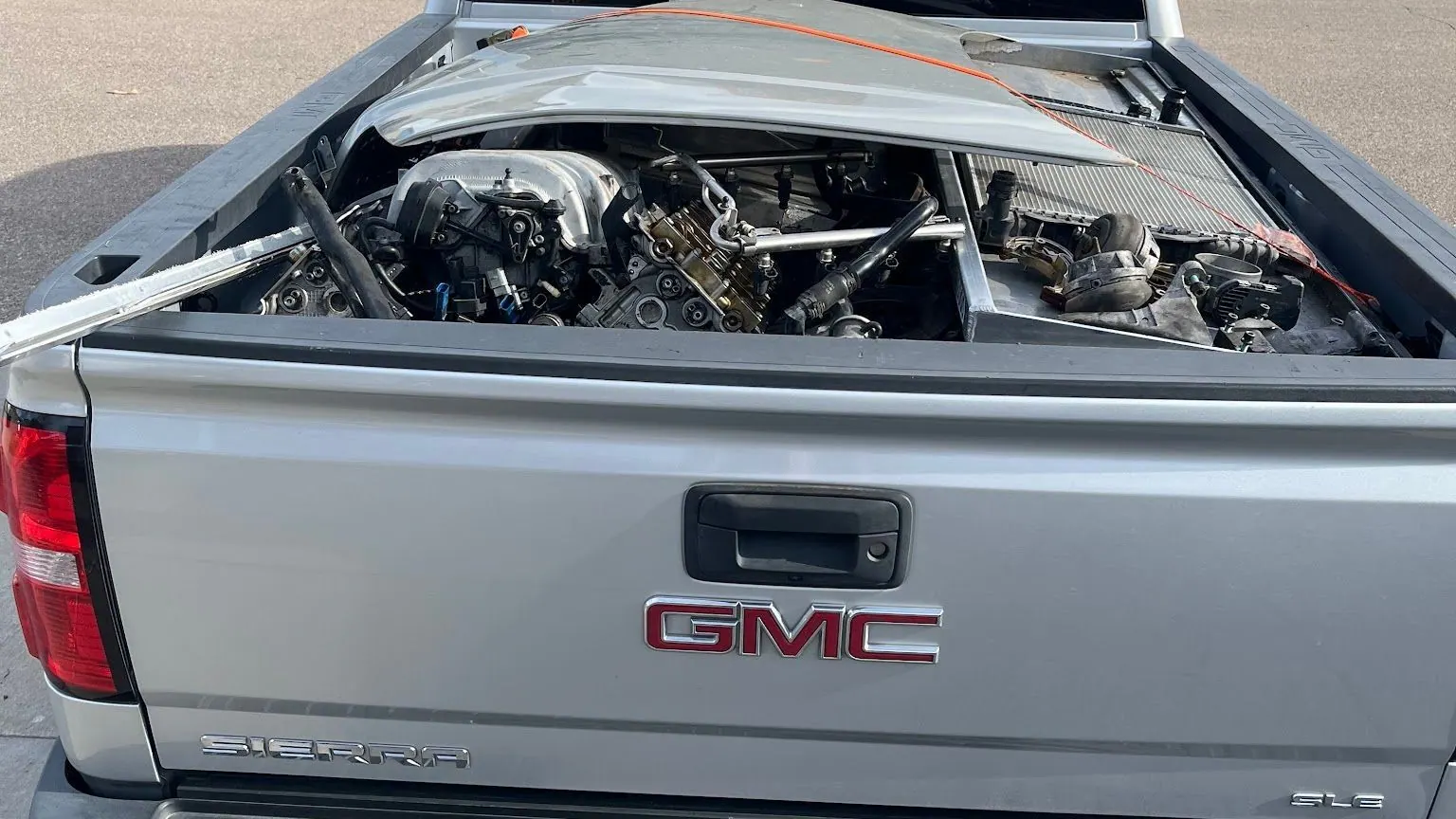 Car engine parts and a bent hood in the bed of a silver GMC pickup