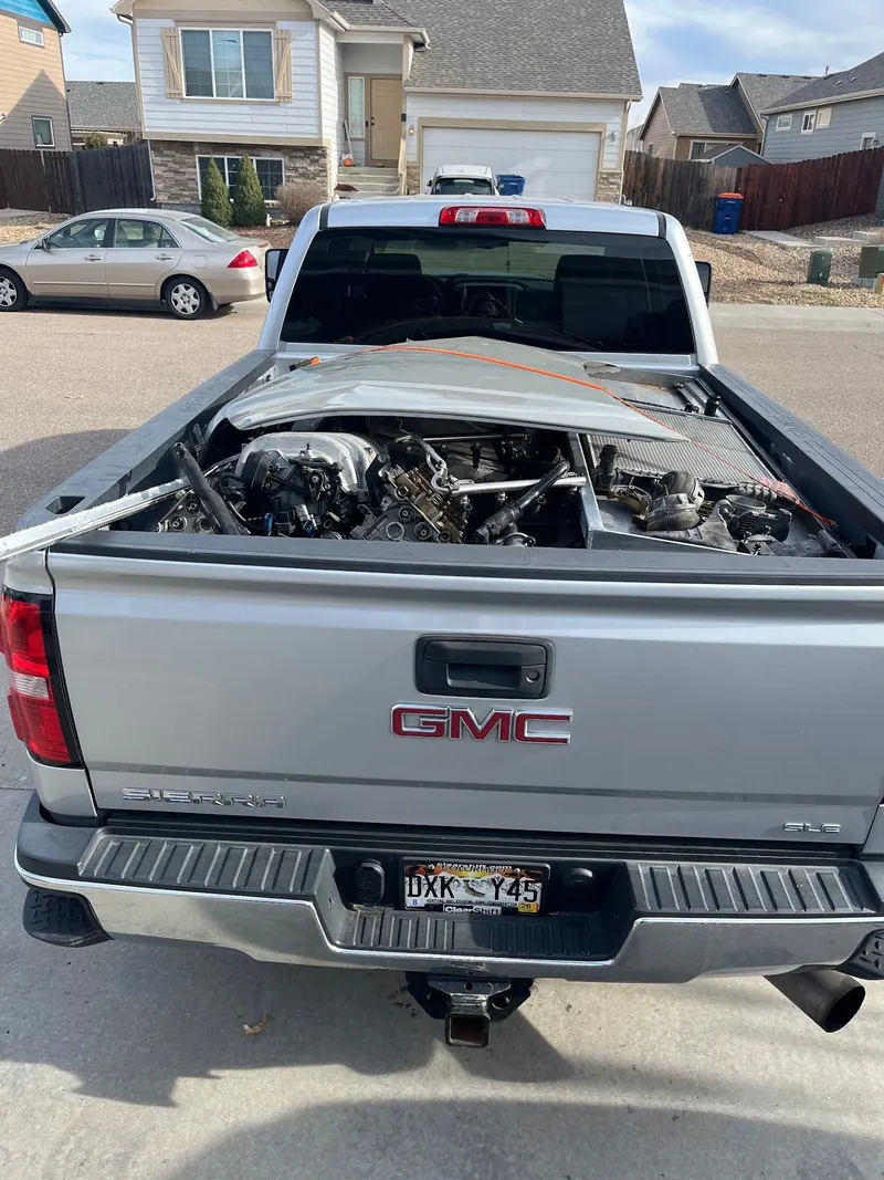 Car engine parts and a bent hood in the bed of a silver GMC pickup