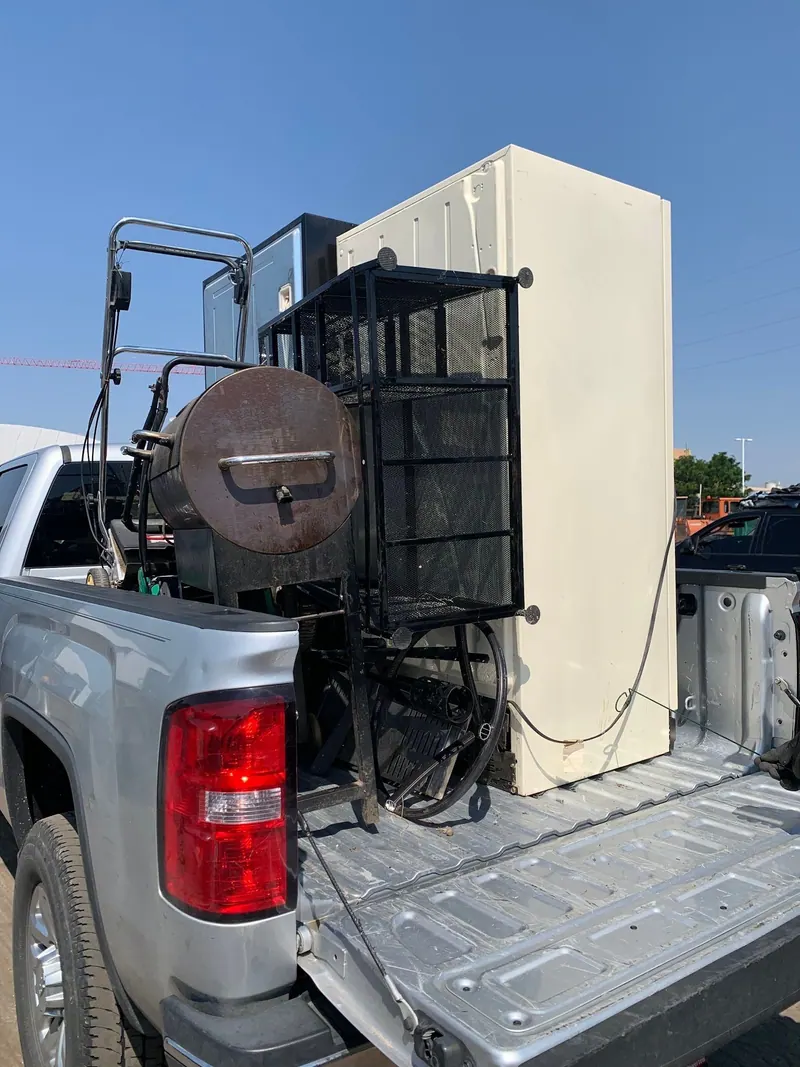 A cream refrigerator, a wire rack and a smoker loaded in the bed of a silver GMC pickup