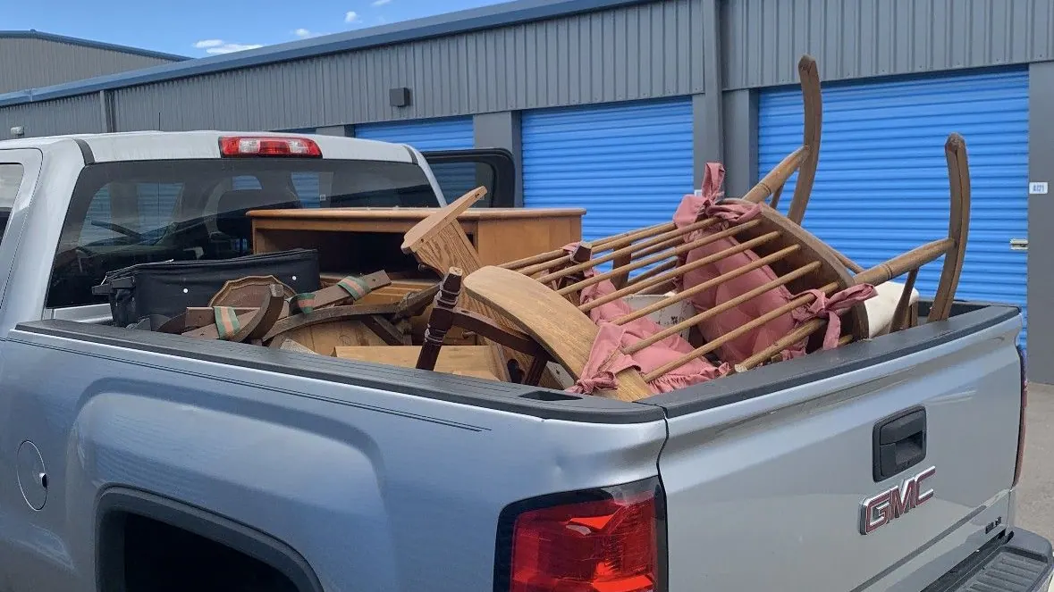 Wooden chairs and a dresser loaded in the bed of a silver pickup