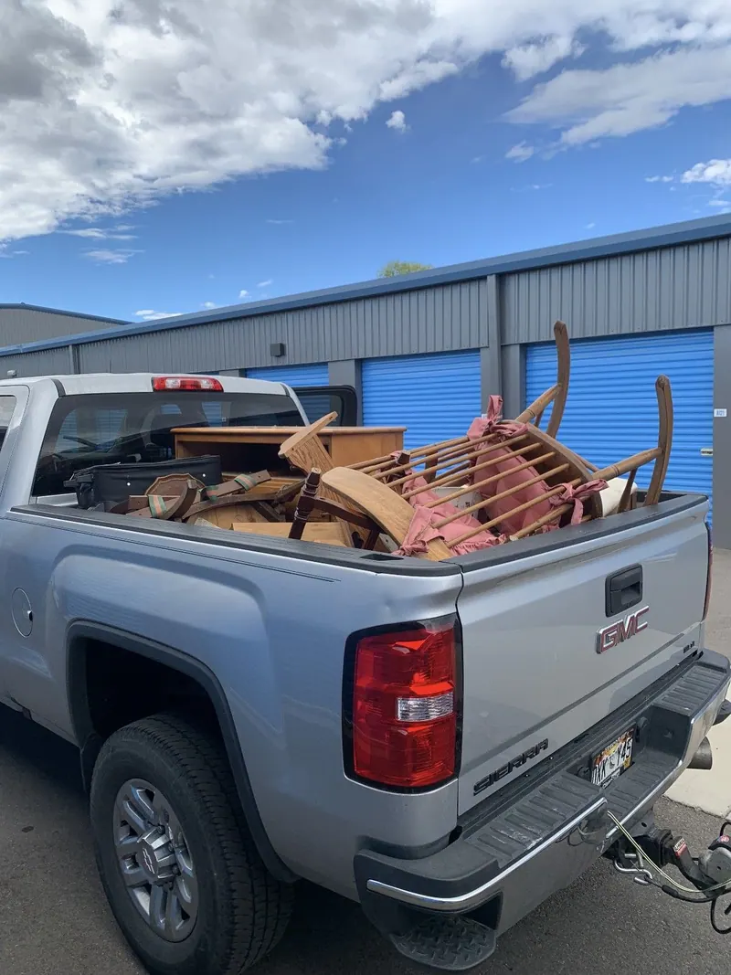 Wooden chairs and a dresser loaded in the bed of a silver pickup