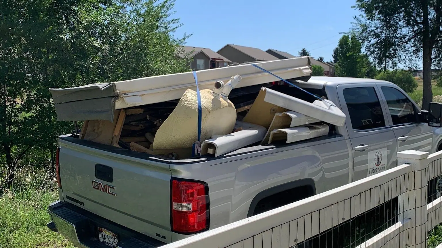 The loaded silver GMC pickup from behind, parked by a white fence