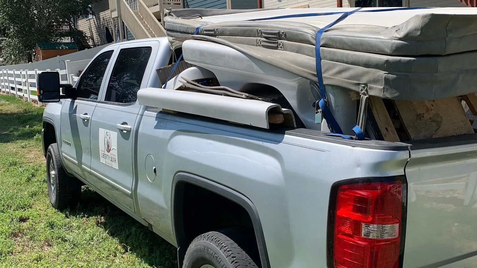 A silver GMC pickup with the Liberty Junk Removal sign on the door and a strapped load in the bed
