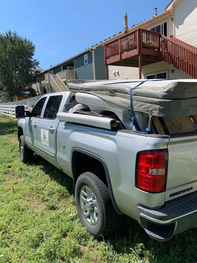 A silver GMC pickup with the Liberty Junk Removal sign on the door and a strapped load in the bed