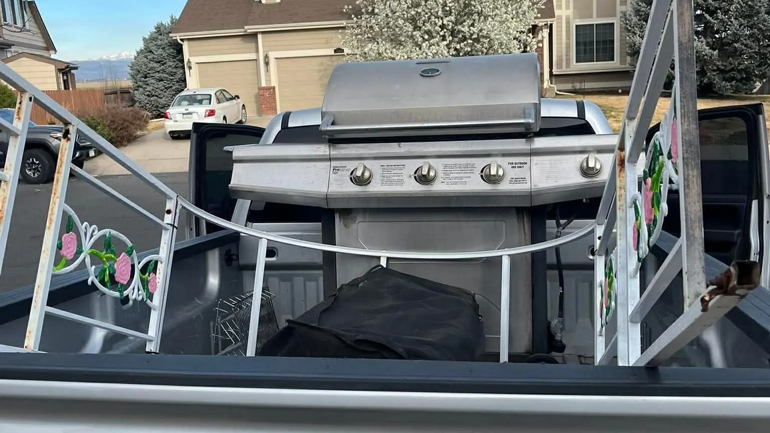 A stainless gas grill and a white metal rack in the bed of a silver GMC pickup