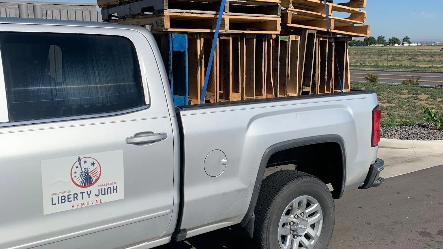 Wooden pallets stacked high in the bed of a silver GMC pickup with the Liberty Junk Removal sign on the door