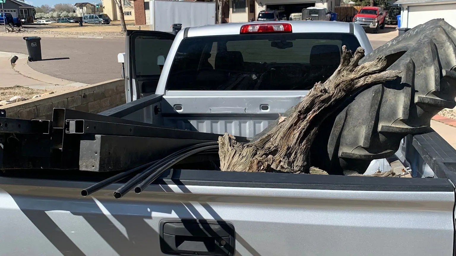 A tree stump, a steel frame and black pipes in the bed of a silver GMC pickup