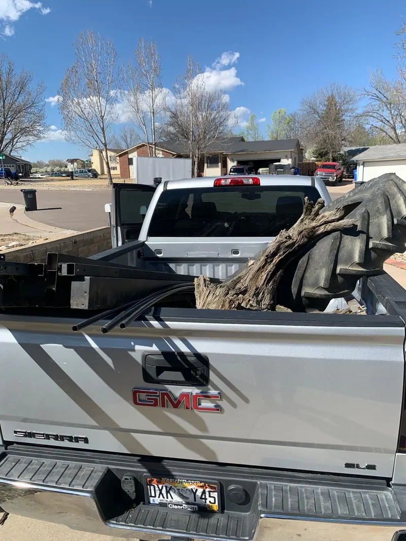 A tree stump, a steel frame and black pipes in the bed of a silver GMC pickup