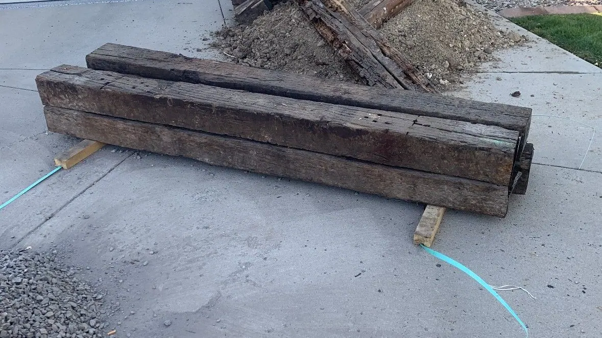 Old wooden timbers and a pile of lumber and dirt stacked on a driveway in front of a garage door