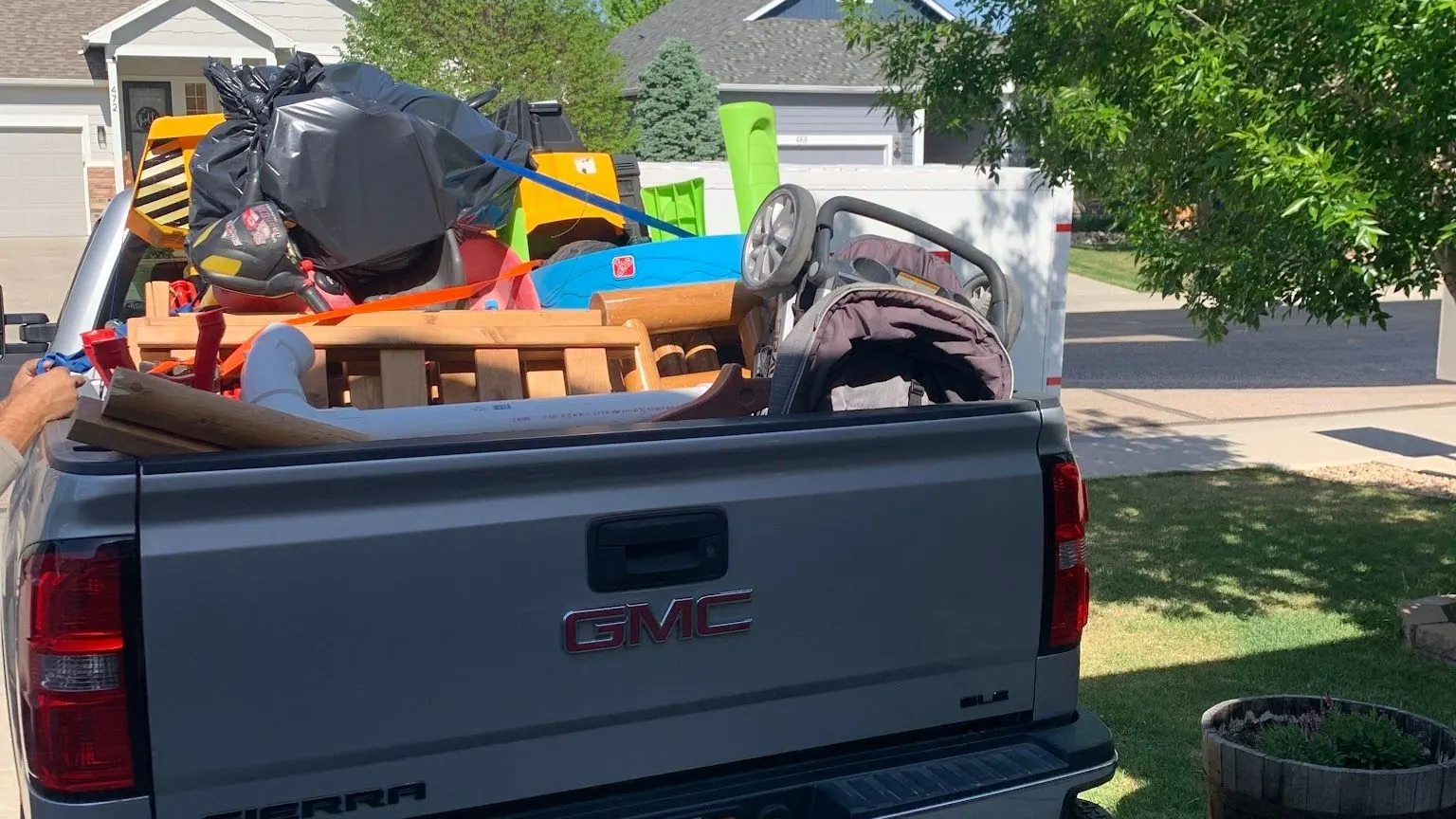 The back of a silver GMC pickup in a driveway with kids' toys piled in the bed