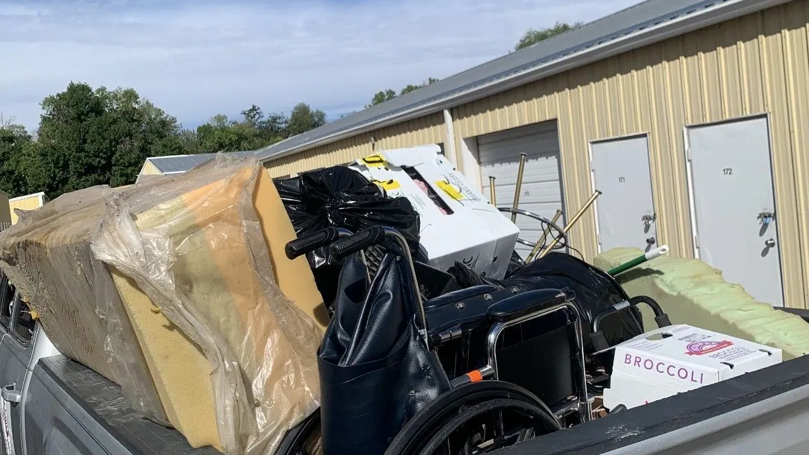 A pickup bed loaded with foam cushions and a wheelchair and trash bags