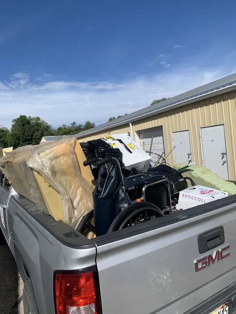 A pickup bed loaded with foam cushions and a wheelchair and trash bags