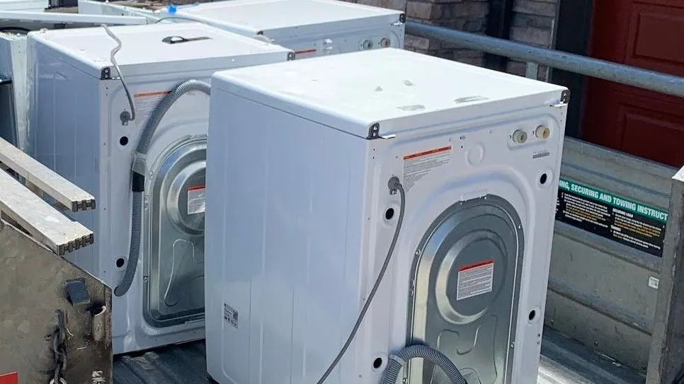White washers and dryers stacked on an open trailer