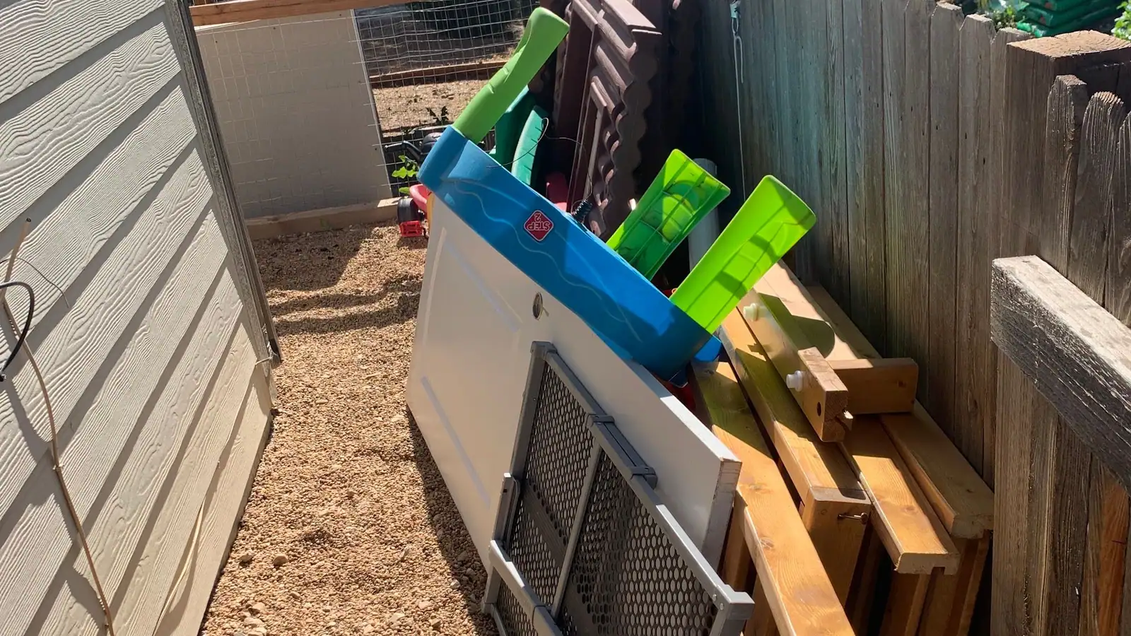 Children's outdoor toys and lumber leaning against a backyard fence
