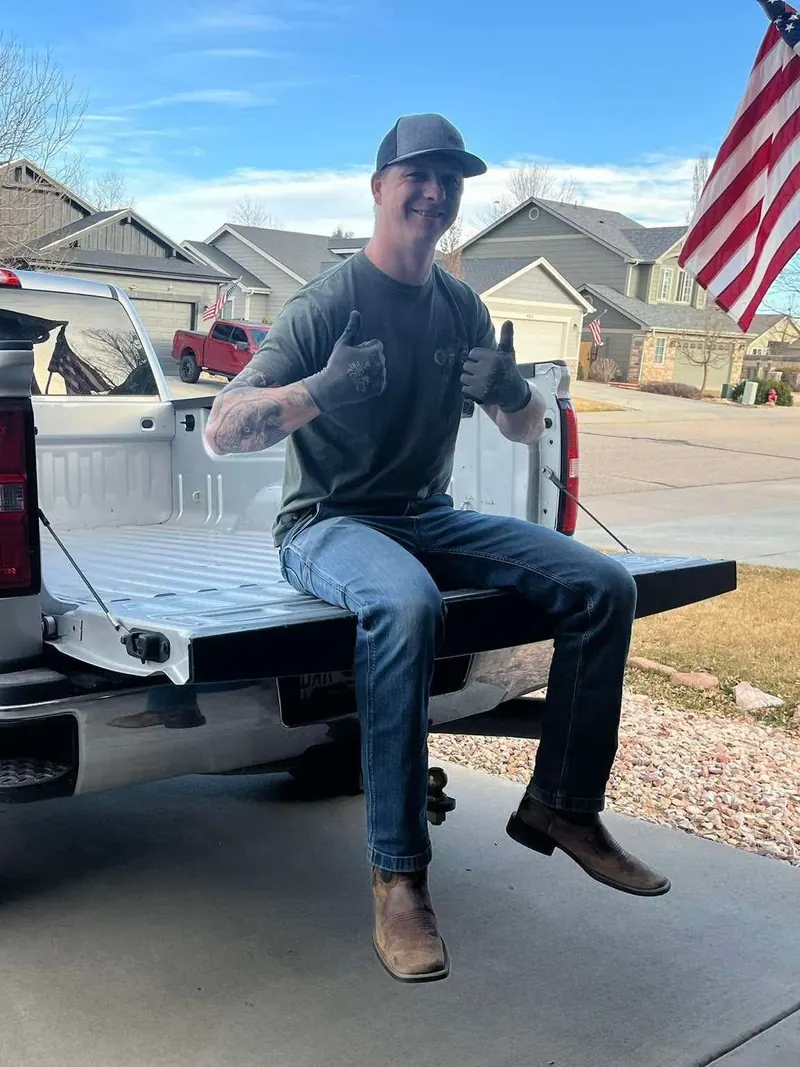 The owner sitting on the tailgate of the silver GMC pickup with an American flag in the background