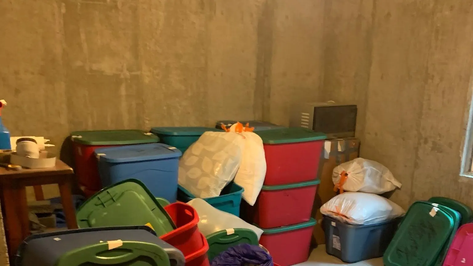 A concrete basement room packed with plastic totes and bags