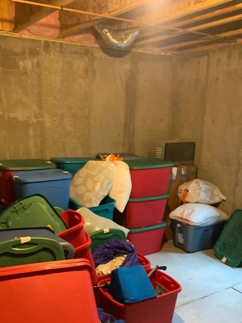 A concrete basement room packed with plastic totes and bags