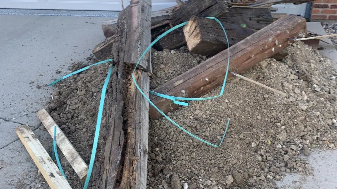 Old wooden posts with wire and dirt piled on a driveway in front of a garage door