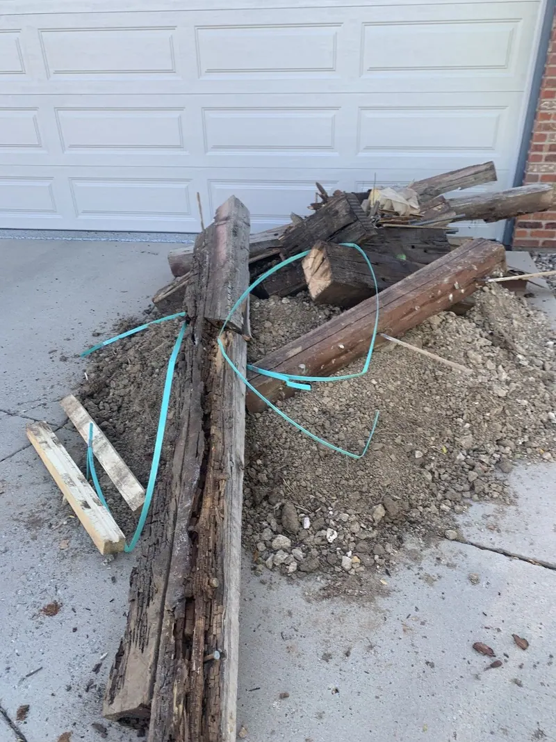 Old wooden posts with wire and dirt piled on a driveway in front of a garage door